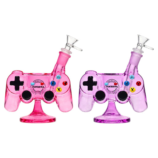 Two Arsenal 7-inch glass game controller bongs in pink and purple, featuring black directional pads, colourful A, B, X, and Y buttons, black joystick details, angled clear glass bowls, and round pedestal bases on a white background.