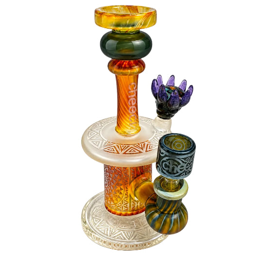 A multi-colored glass water pipe with a tall amber and green stem, a white patterned base, and two smaller bowls, one purple and one blue and green striped, on a white background.