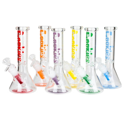 Six clear glass beaker-style water pipes with different colored bases and matching colored internal accents, each printed with the brand name 'Cookies' in a vertical color-matching font. The colors shown are red, orange, yellow, green, and blue. - The Wee Smoke Shop
