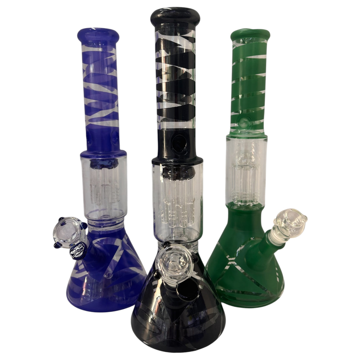 Three spiral stripe glass beaker bongs shown together in blue, black, and green, each with a matching coloured neck, beaker base, clear percolator chamber, angled bowl, and downstem. The Wee Smoke Shop