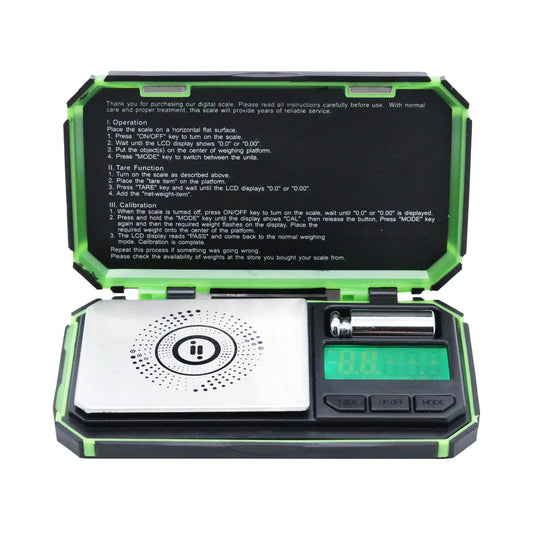 Open Infyniti Nebula digital pocket scale showing stainless steel weighing platform, blue backlit display, control buttons, calibration weight, and instructions inside the lid. The Wee Smoke Shop