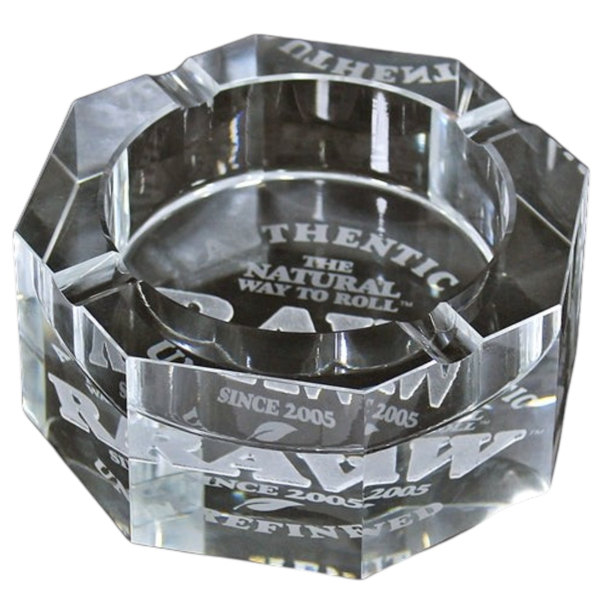 Clear faceted RAW glass ashtray with thick angled sides, built-in cigarette rests, and white “RAW,” “Authentic,” “The Natural Way to Roll,” and “Since 2005” branding visible through the glass. The Wee Smoke Shop