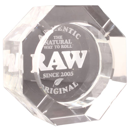 A clear crystal octagonal ashtray featuring a clear circular center printed with the white RAW brand logo and text. The Wee Smoke Shop