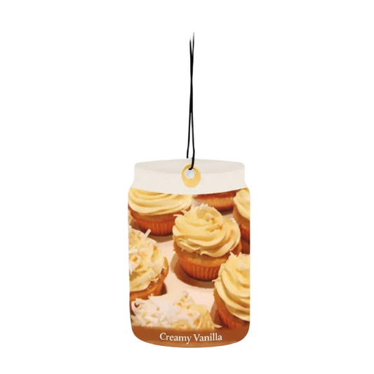 A cylindrical hanging air freshener or scent block labeled 'Creamy Vanilla' with a printed photo of frosted cupcakes on the front, suspended by a black string against a plain white background.