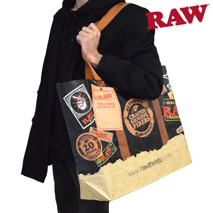 Person holding a Raw branded tote bag with multiple logos on a white background